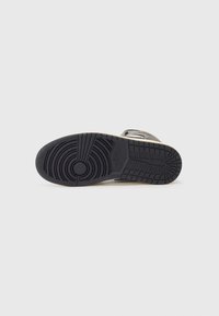 Black rubber shoe sole with circular and linear tread patterns, featuring a Nike logo near the heel and a light-colored edge.