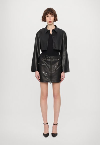 Kratka črna usnjena jakna z gumbnim zapiranjem in dolgimi rokavi, v kombinaciji s črno usnjeno mini krilo z žepi na zadrgo in pasom.
