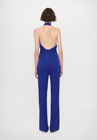 Niebieski kombinezon bez rękawów z halterem przy szyi i odkrytymi plecami. Rozszerzane nogawki o gładkiej fakturze i minimalistycznym designie.
