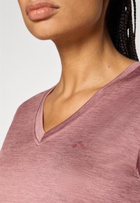 Τοπ με V-λαιμόκοψη και κοντά μανίκια σε ανοιχτό μοβ χρώμα, με υφή στο ύφασμα και διακριτική εκτυπωμένη λεπτομέρεια στην περιοχή του στήθους.