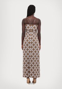 Brown patterned maxi dress with white circular designs, spaghettis straps, and a fitted bodice, ending at the ankles. Smooth fabric texture.