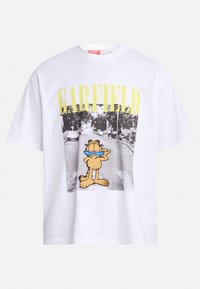 Valge puuvillane T-särk, millel on suur graafika koomilisest kassist, kes kannab prille, ja sõna "GARFIELD" kollases kirjas üleval.