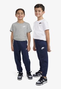 Tricouri Nike gri și albe, asortate cu pantaloni jogger bleumarin. Adidașii au accente negre și gri. Logo-urile sunt imprimate pe piept și pantaloni.