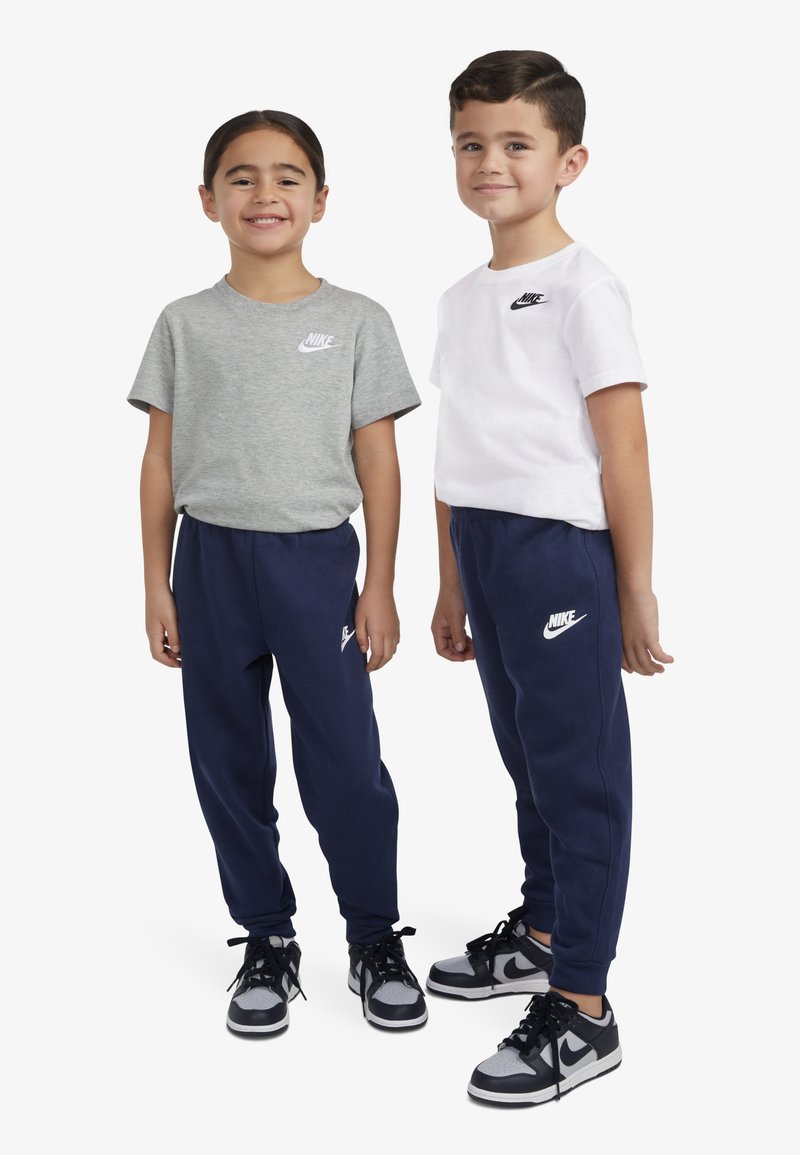 Tricouri Nike gri și albe, asortate cu pantaloni jogger bleumarin. Adidașii au accente negre și gri. Logo-urile sunt imprimate pe piept și pantaloni.