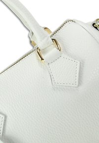 White leather handbag close-up, featuring a textured finish, gold hardware, and a diamond-shaped leather accent with stitching details.