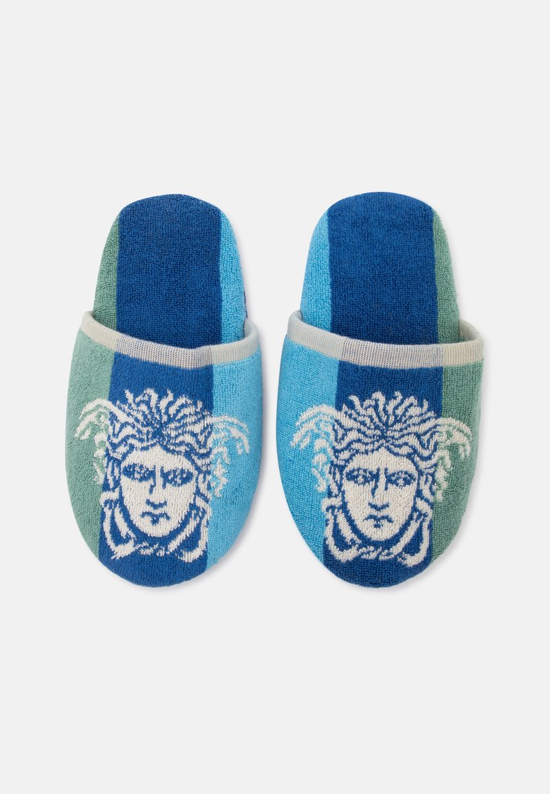 Pair of blue and green striped slippers with a white Medusa head design on the front, made of soft textured fabric.