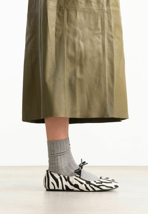 Unterschenkel mit grauen Socken und schwarz-weißen Ballettschuhen mit Zebramuster und Schleife, kombiniert mit einem knielangen olivgrünen Rock.