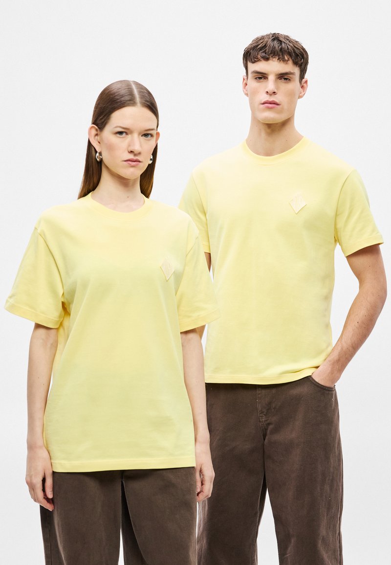 T-shirt di cotone giallo a maniche corte, con un piccolo logo a diamante testurizzato sul petto. Abbinate a pantaloni marroni.
