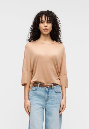 Světlohnědý volný top s tříčtvrtečními rukávy, kombinovaný s vysokým pasem na světle modrých džínách a hnědým páskem. Hladká textura.