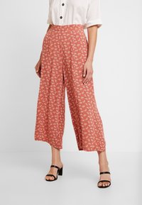 Pantalons à jambes larges de couleur rouille, ornés d'un délicat motif floral blanc. Confectionnés en tissu léger, avec une texture lisse et une taille haute.