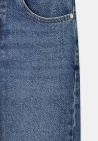 Tissu denim bleu avec des coutures visibles et un petit coin de poche avant avec un rivet métallique sur un jean.
