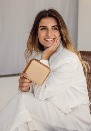 Tan leather wallet with a zippered closure, featuring a beige front and embossed logo, held by a person wearing a white outfit.