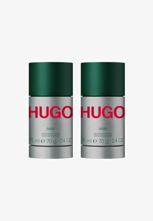 To deodorantstænger med grønne låg og sølvbaser. Etiketternes indhold inkluderer rød tekst og detaljer: "HUGO MAN," "75 ml," "70 g," og "24 OZ."