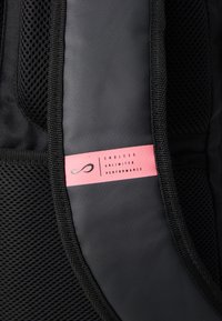 Fekete hátizsák, hálós panellel és sima résszel. Egy rózsaszín címke hirdeti az "ENDLESS UNLIMITED PERFORMANCE" feliratot egy logóval.