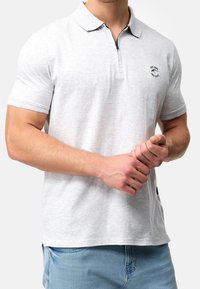 Polo shirt grigio chiaro con colletto, maniche corte e un piccolo logo sul petto. Presenta un accento blu navy al colletto.