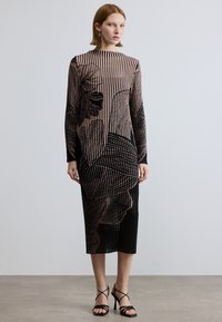 Robe mi-longue à rayures noires et nude avec motifs floraux, manches longues et silhouette droite. Associée à des talons noirs à brides.