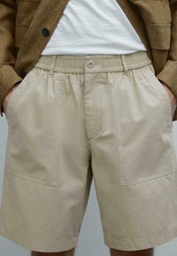 Beige katoenen shorts met een elastische tailleband, voorzien van twee zijzakken en een knoopsluiting, met een gladde textuur en een ontspannen pasvorm.