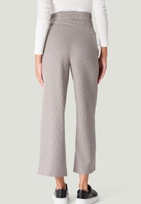 Pantalons taille haute, à jambe large, dans un motif pied-de-poule beige atténué, avec une texture lisse et des poches latérales, associés à des baskets noires.