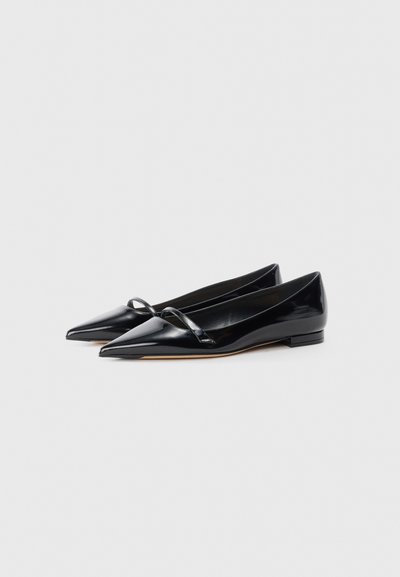 Black patent leather flats with a pointed toe, featuring a thin strap across the instep and a low, square heel. Smooth texture, minimalist design.