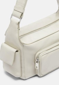 Borsa a tracolla in pelle crema con scomparto principale con zip, tasca frontale con accessori in argento e tracolla regolabile.