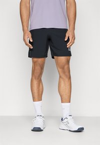 Calções de atletismo pretos com um corte ajustado, tecido leve e detalhe do logótipo na lateral, combinados com meias brancas e sapatos brancos.