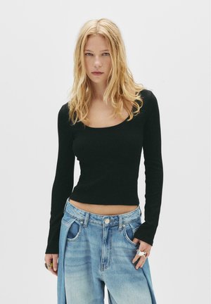 Black ribbed long-sleeve shirt with a scoop neckline, paired with loose light blue denim jeans. The outfit features a relaxed fit and minimal details.