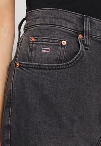 Tmavě šedé džíny z denimu s měděnými detaily, které mají malé vyšívané logo na zadní kapse a klasický pětikapsový design.