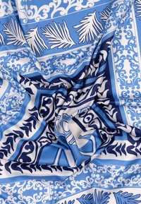 Tissu coloré présentant un motif géométrique bleu et blanc avec des motifs de feuilles, une texture lisse et un design doux et fluide.