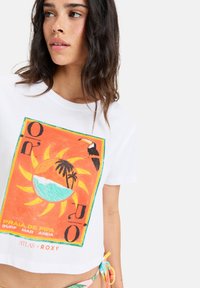 White cropped t-shirt featuring a colorful graphic with a sun, waves, palm trees, and a toucan. Soft cotton material with short sleeves.