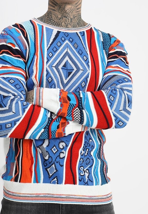 Pull en tricot multicolore avec des motifs géométriques en bleu, rouge et blanc, doté de poignets côtelés et d'un col rond.