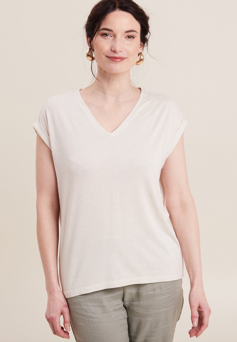 Helles beige V-Ausschnitt-T-Shirt mit kurzen, umgeschlagenen Ärmeln, aus einem strukturierten Stoff mit feinen Streifen, kombiniert mit hellen Hosen.