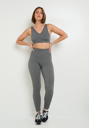 Ensemble de soutien-gorge de sport et de leggings assortis gris, fabriqué en tissu doux, présentant un design en V, une coupe ajustée, et associé à des chaussures de sport noires.