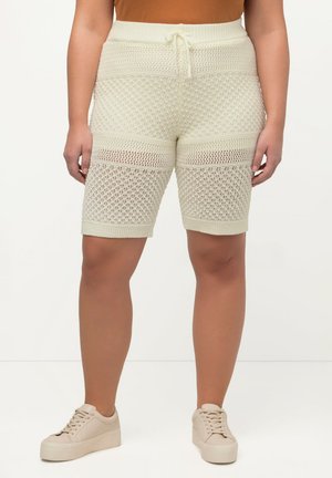 Shorts crema a maglia con motivo a trama aperta, vita con cordoncino e polsini a costine. Abbinati a sneakers beige su uno sfondo chiaro.