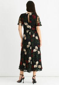 Black floral midi dress with sheer sleeves, featuring red and beige embroidered roses and a back keyhole. Accompanied by black strappy heels.