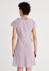 Blumengemustertes Kleid in Pink mit kleinen schwarzen und roten Akzenten. Kurze Ärmel und ein rüschengestalter Kragen. Ausgestellter Saum in Oberschenkelhöhe.