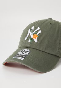 Olijfgroene pet met geborduurd wit "NY" logo en bloemenontwerp, voorzien van een zichtbaar merklabel met de tekst "47 Clean Up, Verstelbaar."