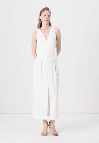 Rochie albă, fără mâneci, cu decolteu în V, lungime până la glezne, cu o fanta în față și pliseuri. Pur tată cu sandale bej cu vârful deschis.