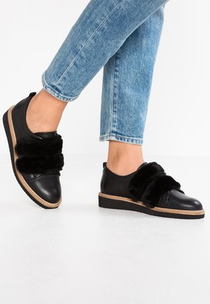 Sorte lædersneakers med en kraftig sål, der har et blødt sort bånd på tværs foran og tan detaljer rundt om sålen.