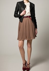 Chaqueta de cuero negra sobre una blusa crema, combinada con una falda plisada color topo y tacones burdeos. Incluye un cinturón rojo para darle un toque.