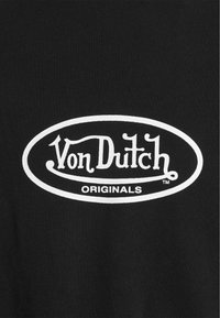 Camiseta de algodón negra con un gran logo ovalado blanco que incluye el texto "Von Dutch" y "ORIGINALS", exhibido de manera prominente en el centro.