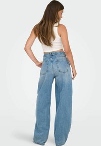 Traperice s visokim strukom i širokim nogavicama u plavoj boji s izblijeđenim završetkom. Imaju pet džepova i kopčanje na gumb, izrađene su od denim tkanine.