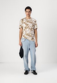 Brun og hvid mønstret t-shirt med korte ærmer, parret med lyseblå denim jeans og sorte sko, bærende på en sort taske.