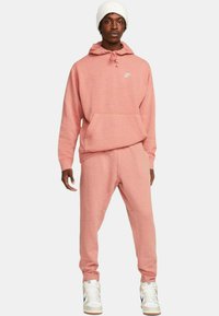 Różowy polarowy Hoodie z przednią kieszenią i troczkami, w zestawie z pasującymi spodniami dresowymi. Zawiera małe białe logo i ściągacze przy mankietach.