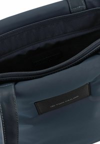 Sac bleu marine avec un extérieur lisse, doté d'un dessus zippé, d'accents en cuir et d'une étiquette de marque tissée à l'intérieur.