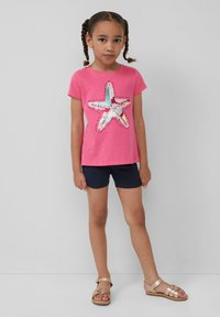 Roze katoenen T-shirt met een sterontwerp van pailletten, gedragen met marineblauwe shorts en gouden sandalen. Eenvoudige ronde hals en korte mouwen.