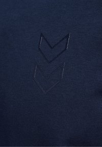 Granatowy materiał o teksturowanej, prążkowanej powierzchni. Posiada ciemny haftowany logo w kształcie chevronu, umieszczone na środku, z subtelnymi detalami ściegów.