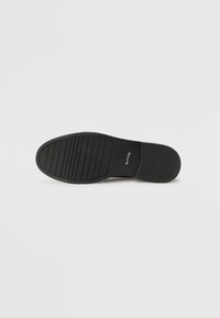 Black shoe sole featuring a smooth, flat design with horizontal grooves for traction. Includes a slight raised edge at the heel.