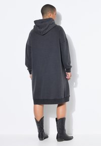 Übergroßes dunkelgraues Hoodie-Kleid mit gerippten Bündchen und Saum, ausgestattet mit einer großen Kapuze und Seitentaschen, kombiniert mit schwarzen Cowboy-Stiefeln.