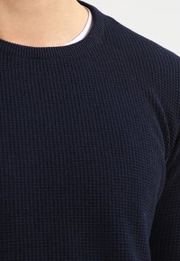Granatowy sweter o fakturowanej powierzchni, z prążkowanym wzorem, okrągłym dekoltem i krótkimi rękawami, wykonany z miękkiego, tkanej tkaniny.