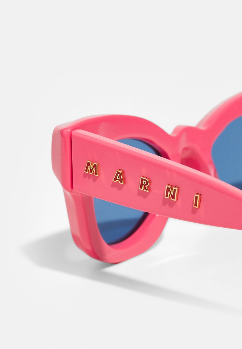 Gafas de sol de plástico rosa con lentes azules. Presenta letras doradas en relieve que dicen "MARNI" en las patillas. Diseño audaz y angular.